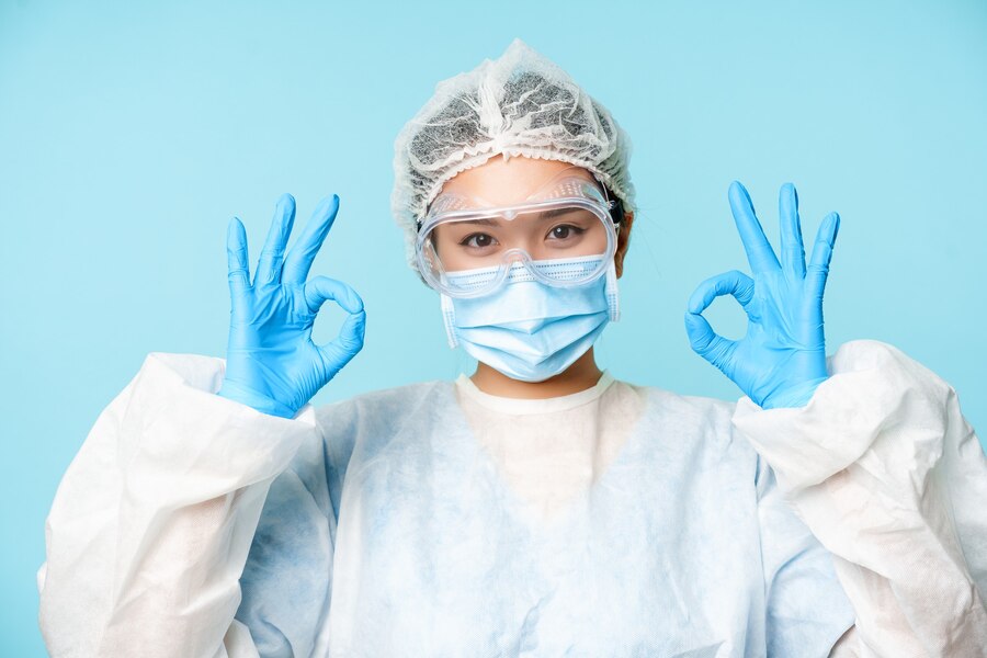 Healthcare worker wearing blue nitrile gloves making an ‘OK’ gesture with their finger
